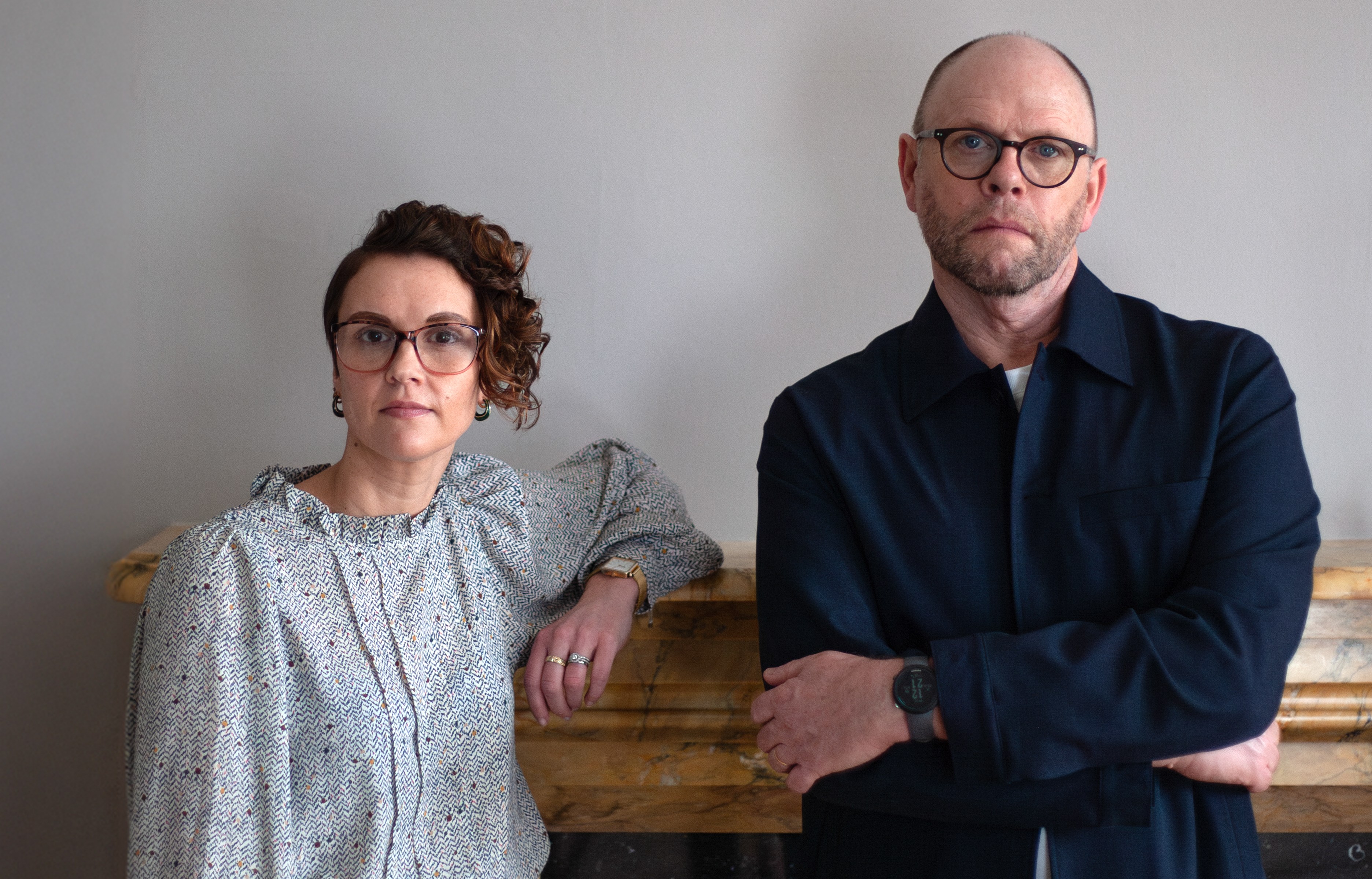 Portrait of two people standing by a fireplace.