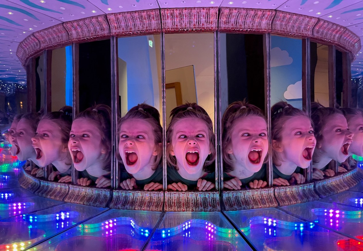 Multiple reflections of a girl shouting in a mirrored science museum exhibit.