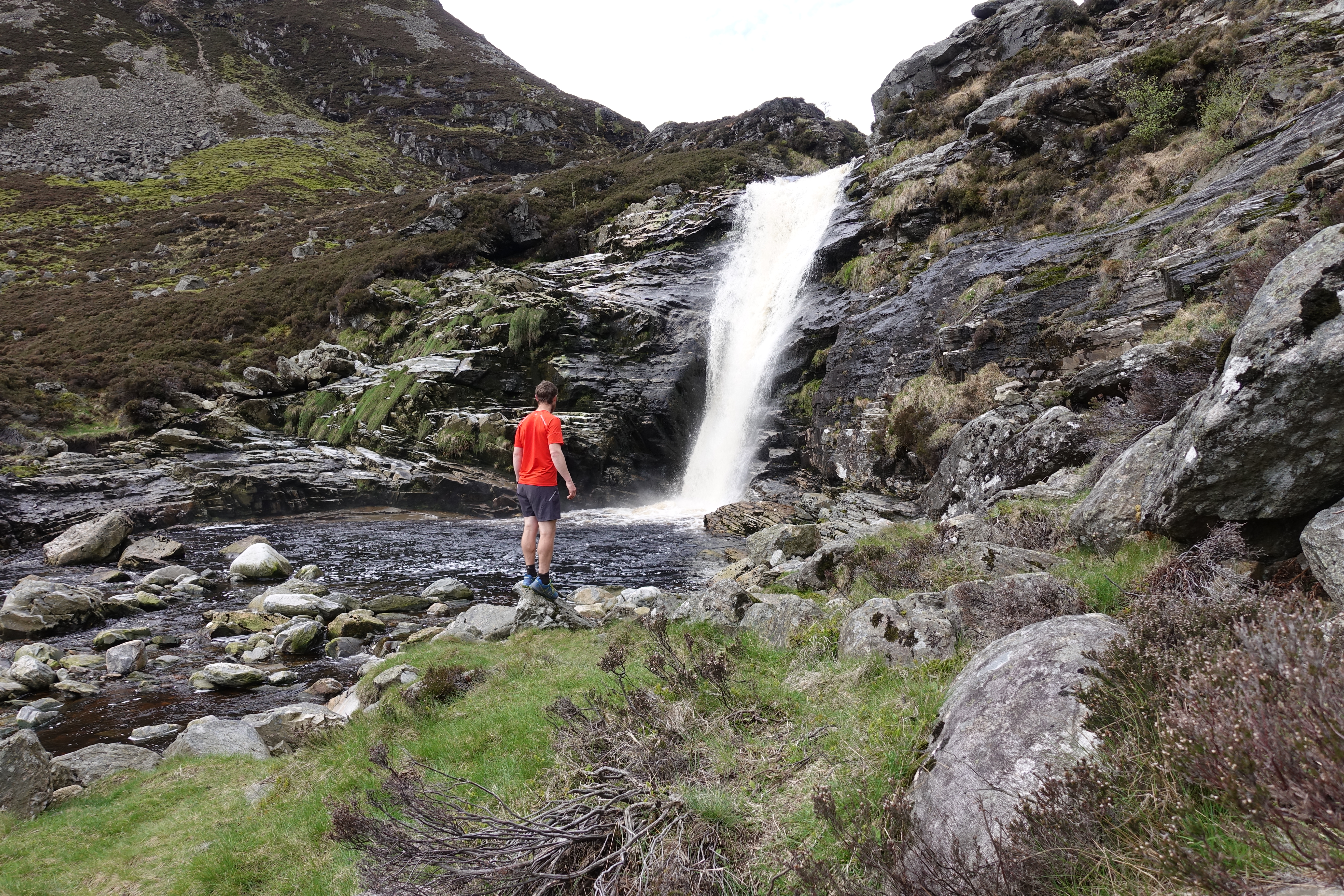 Person standing near waterfall in rocky landscape.