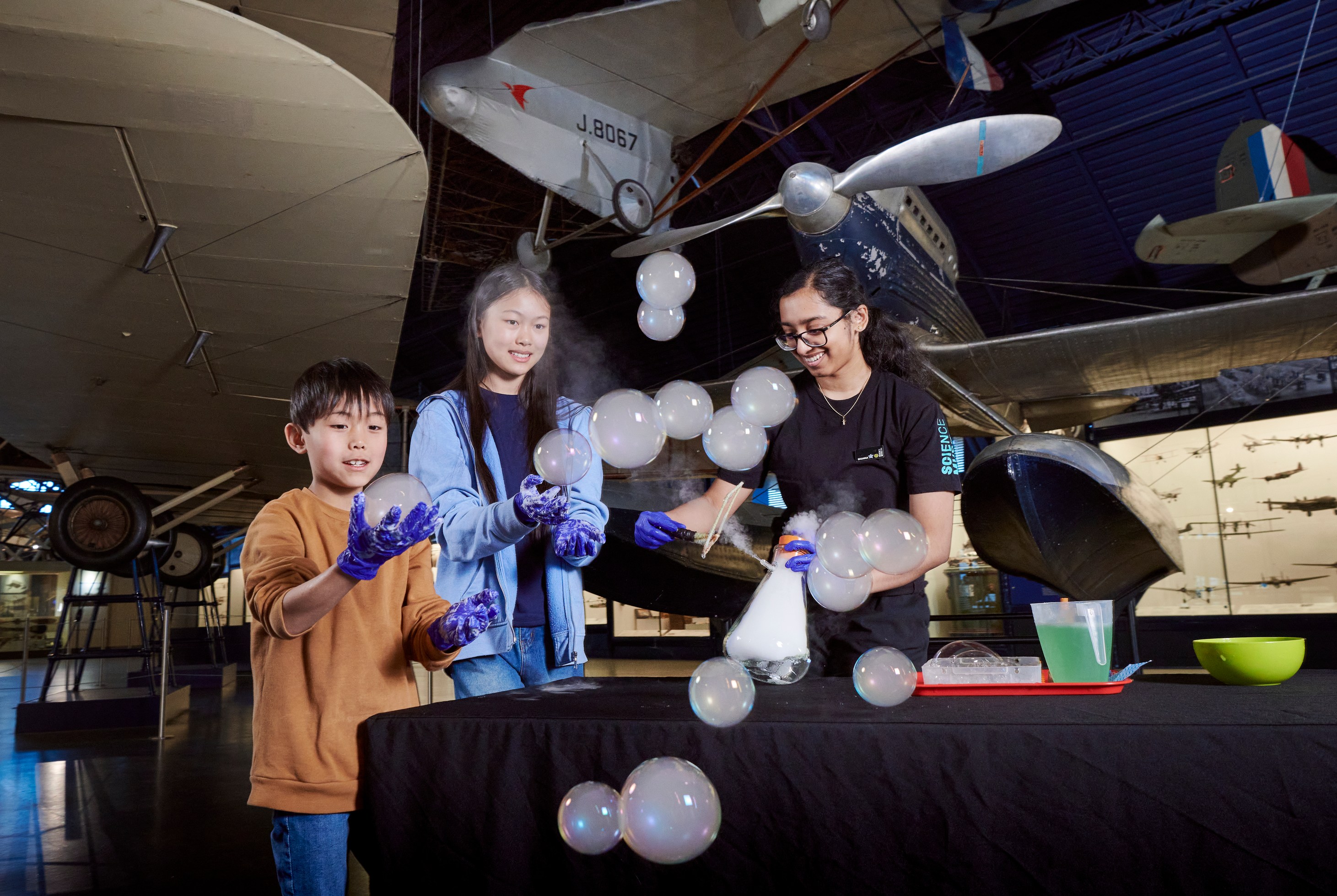 Three children and a Science Museum explainer making large bubbles in the Flight gallery.