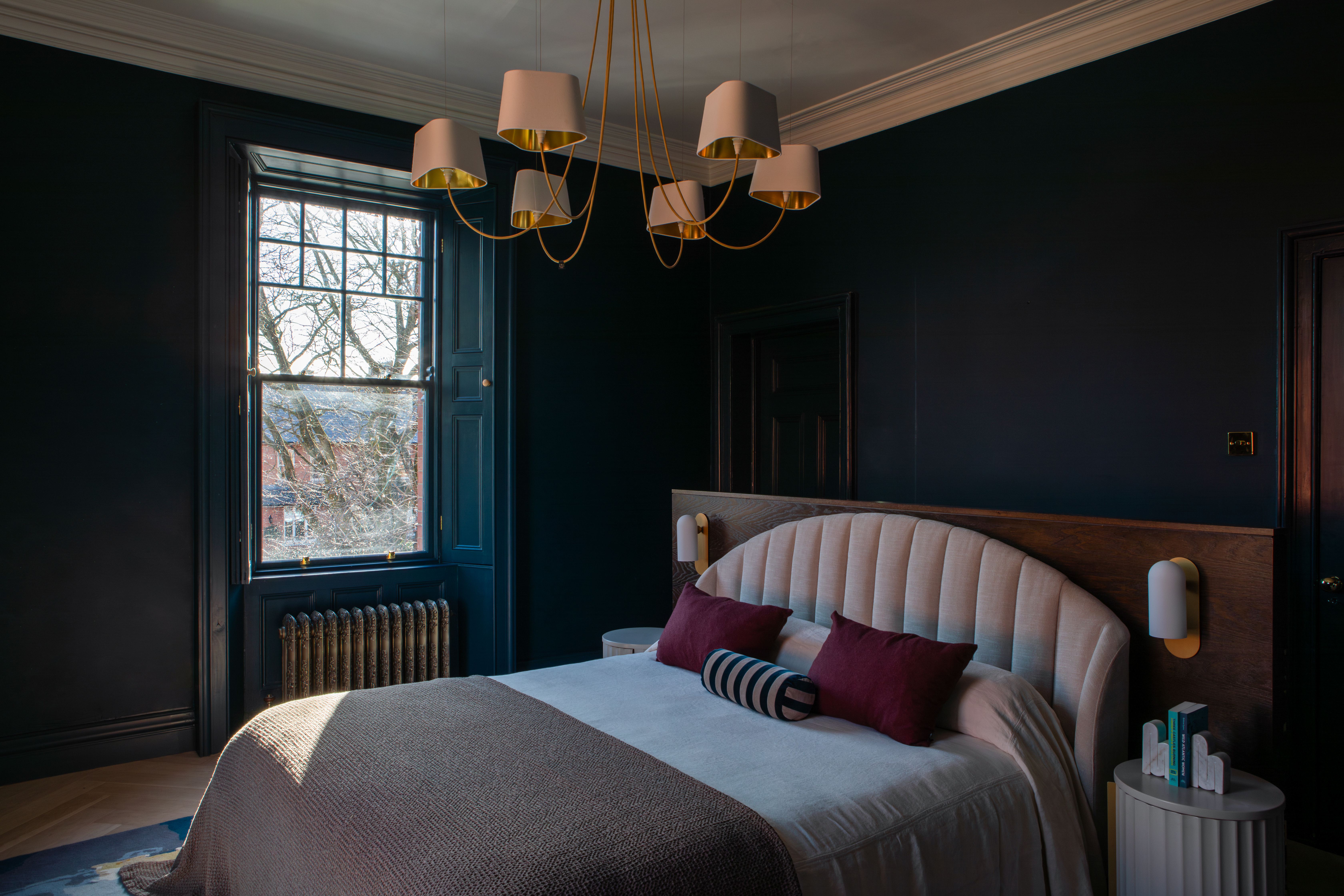 Bedroom with a large bed, dark walls, and a gold chandelier.