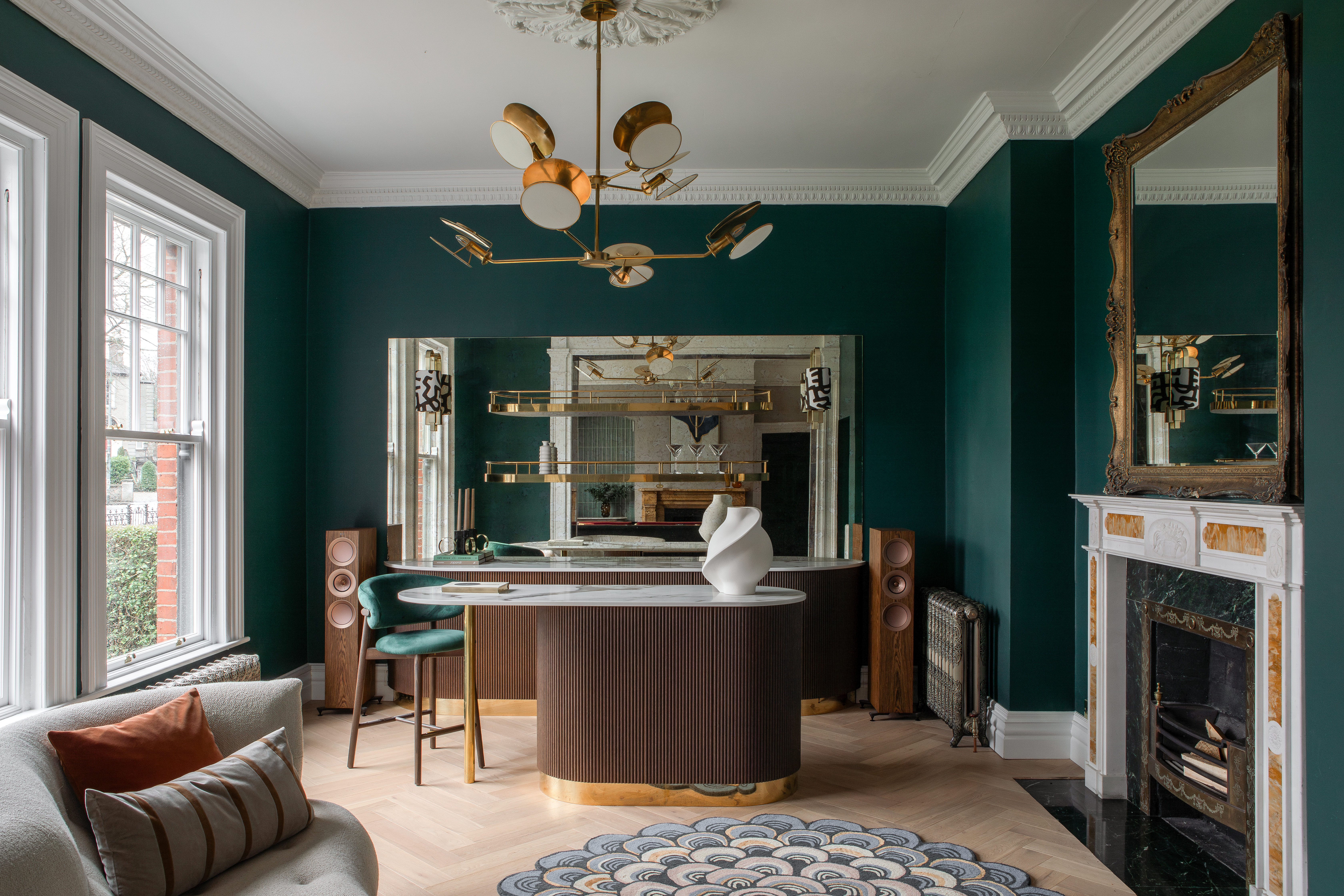 Interior view of a home bar with dark green walls, a marble-topped bar, and a decorative rug.